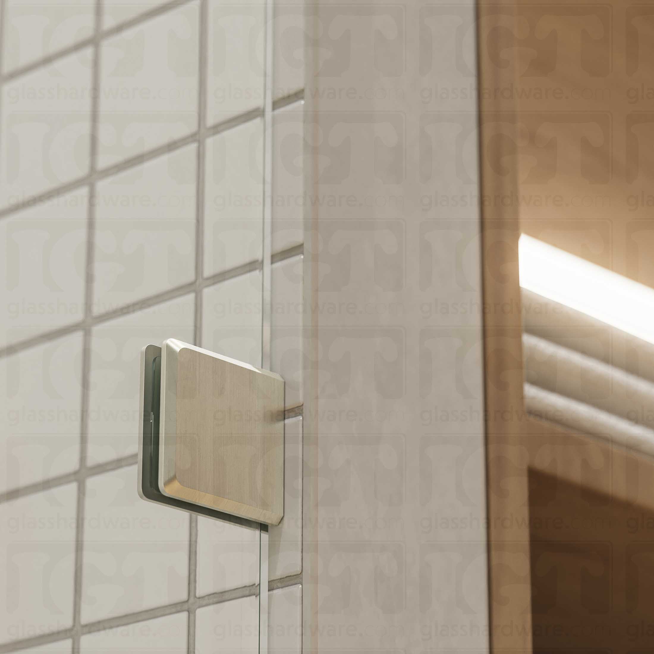 A close-up of a Wall-to-Glass Bilboa Clamp mounted to the shower's tile wall. The clamp is securely holding the shower's fixed glass panel in place. Brushed Nickel.