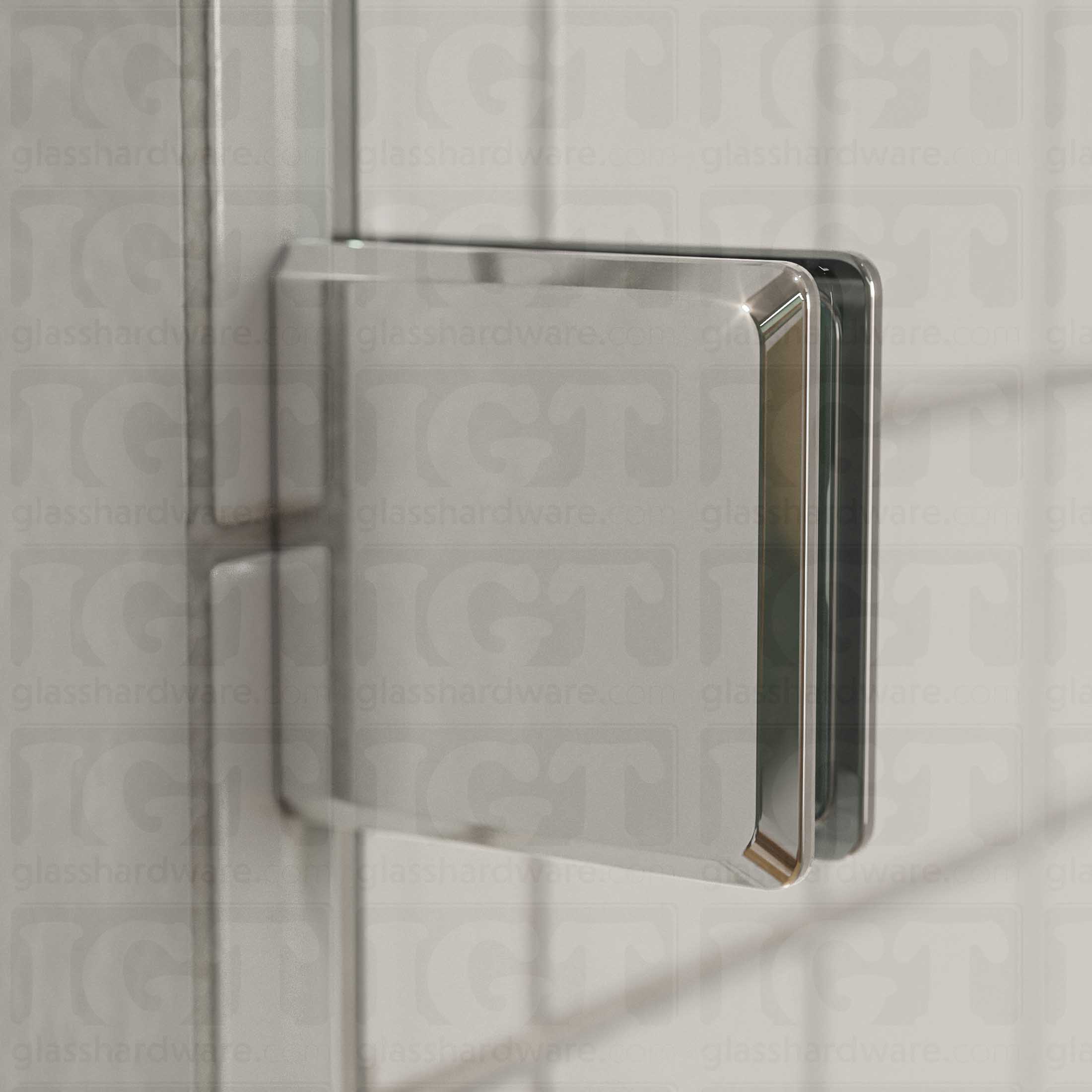 Close-up view of a Wall-to-Glass Bilboa Clamp mounted to the shower's white tile wall. Natural light from the shower window reflects off the clamp's beveled edges. Chrome Polished.