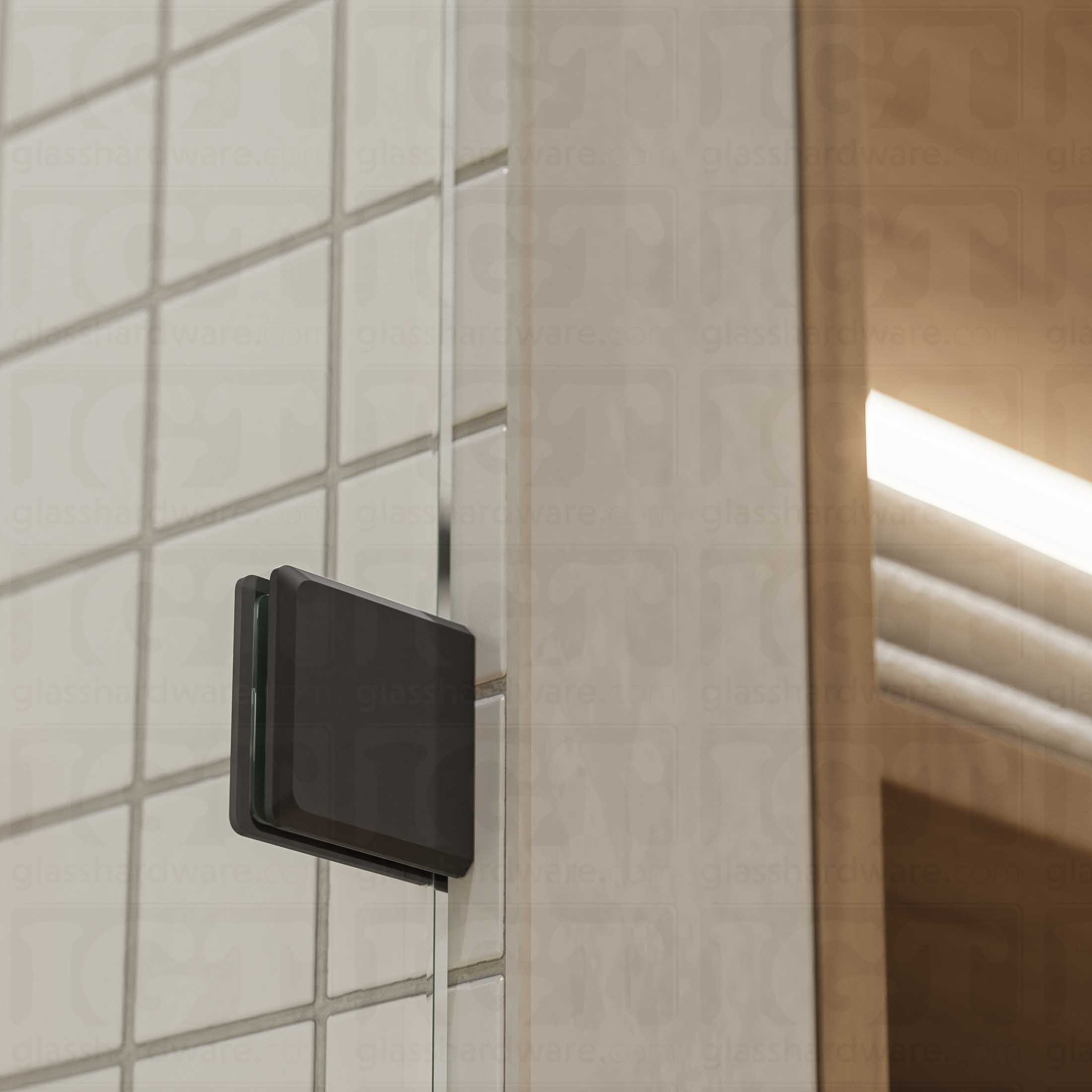 A close-up of a Wall-to-Glass Bilboa Clamp mounted to the shower's tile wall. The clamp is securely holding the shower's fixed glass panel in place. Matte Black.