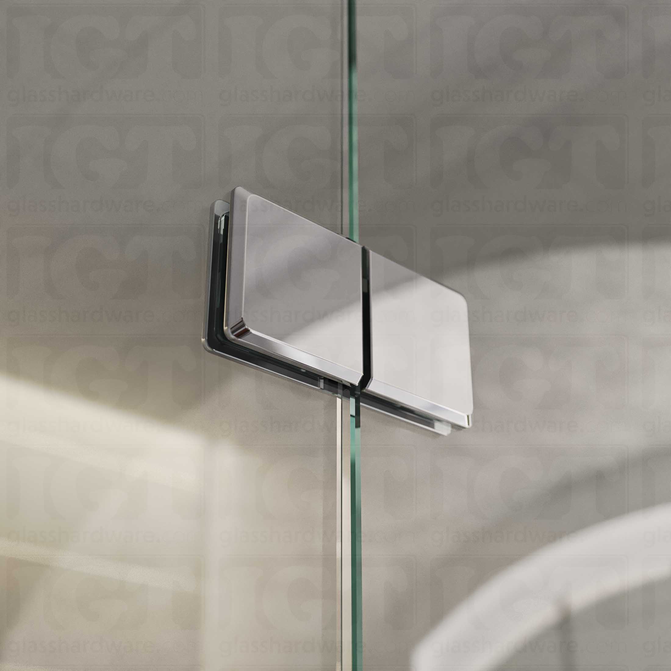 A close-up view of the Glass-to-Glass 180 Degree Bilboa Clamps (Split Face), installed on a frameless glass shower enclosure. Natural light travels along the clamp's sleek beveled edges and adds dimension to its overall design. Chrome Polished.