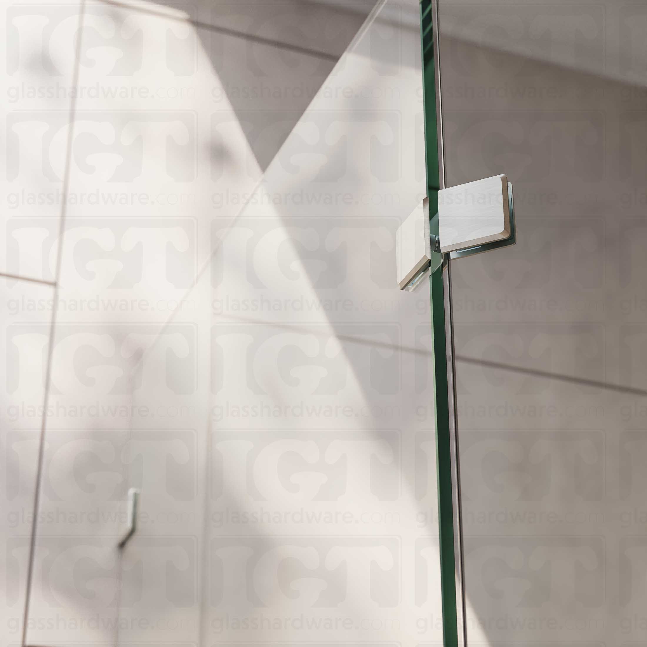 A close-up view of the Glass-to-Glass 135 Degree Bilboa Clamp, installed on a neo angle shower enclosure. Natural lighting showers in from the bathroom's window, and glistens along the clamp's sleek beveled edges. Brushed Nickel.