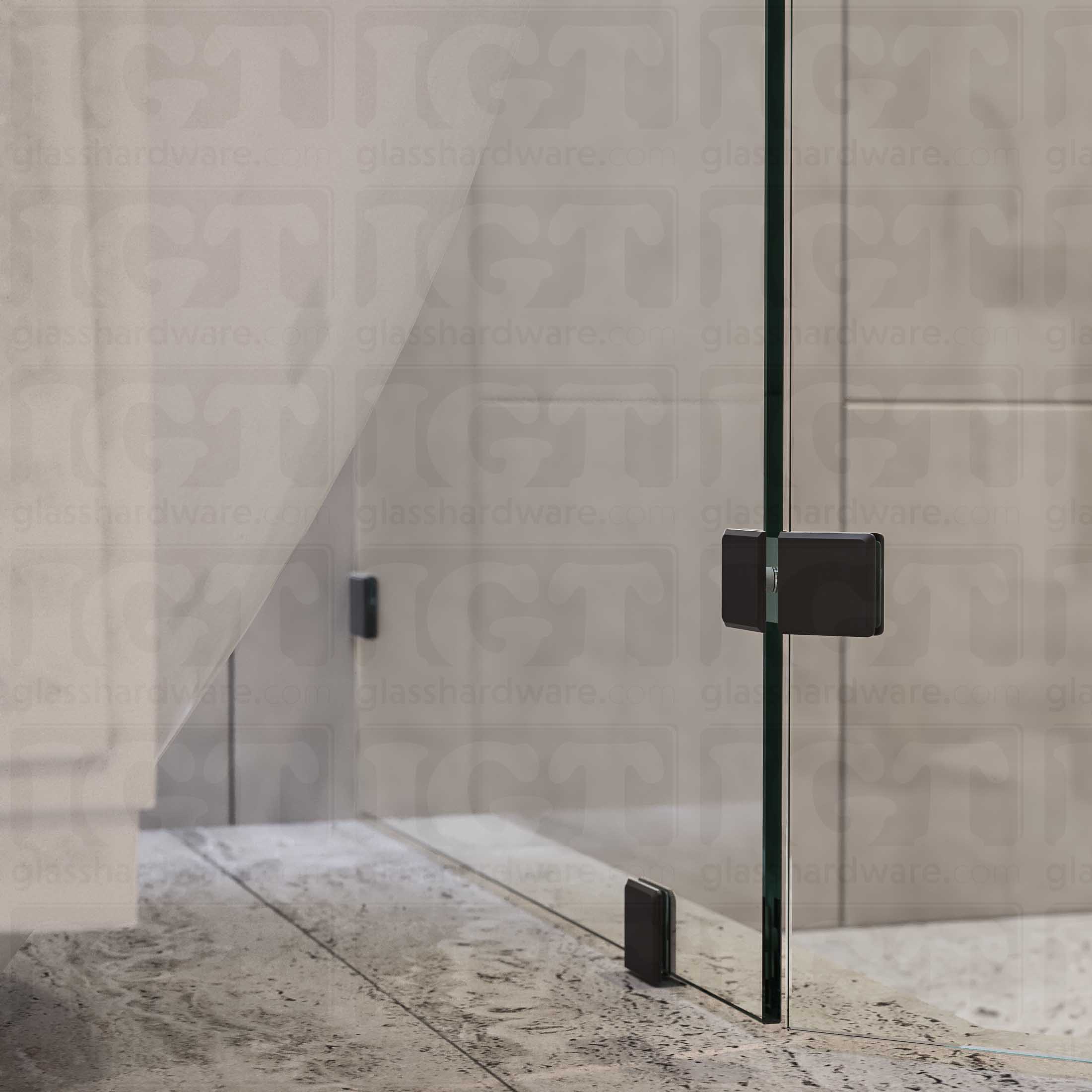 A bottom view of the neo-angle shower's fixed panels, secured by a floor mounted clamp, a wall mounted clamp, and the Glass-to-Glass 135 Degree Bilboa clamp. The shower's look is enhanced by the hardware's matching finish and beveled-edge design. Matte Black.