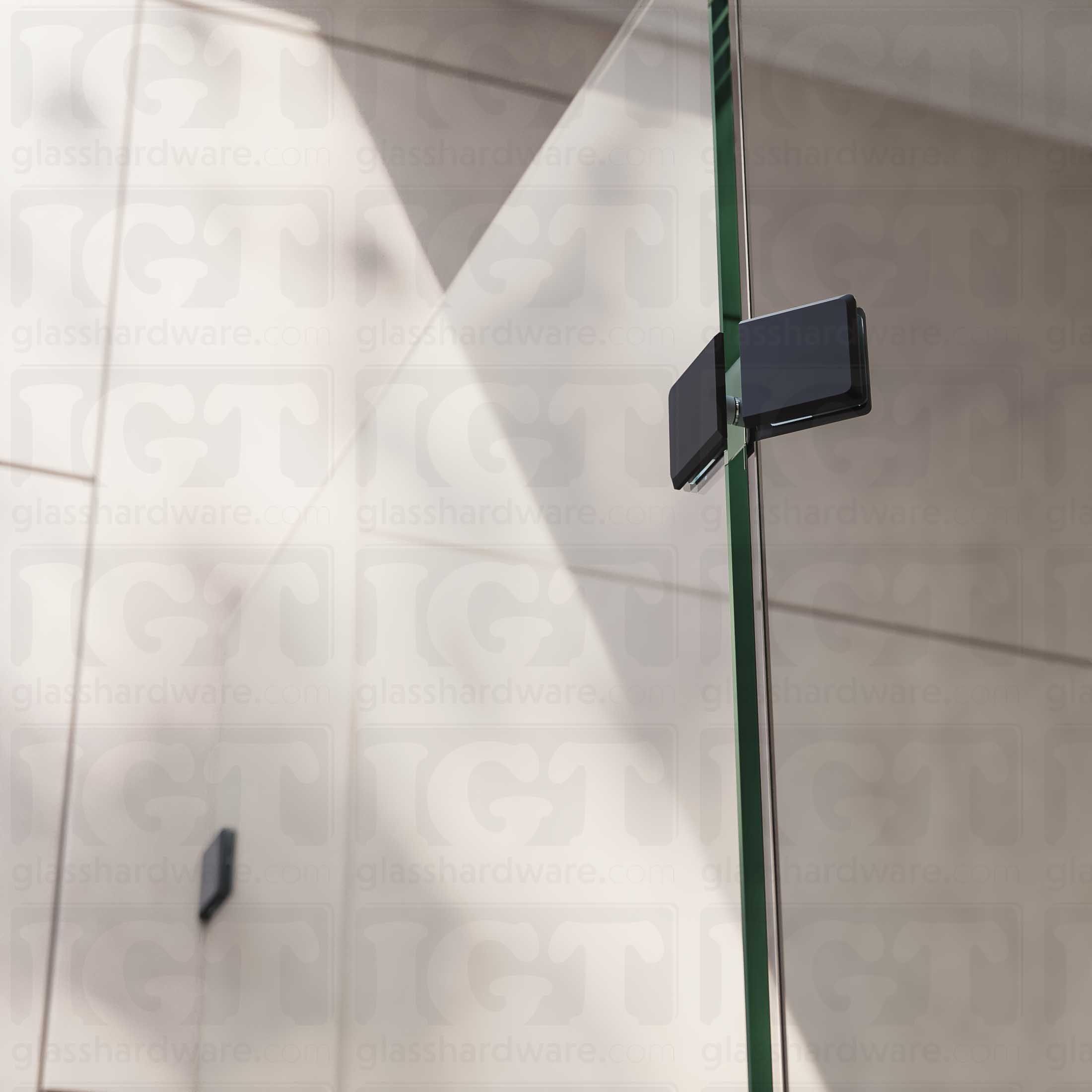 A close-up view of the Glass-to-Glass 135 Degree Bilboa Clamp, installed on a neo angle shower enclosure. Natural lighting showers in from the bathroom's window, and glistens along the clamp's sleek beveled edges. Matte Black.