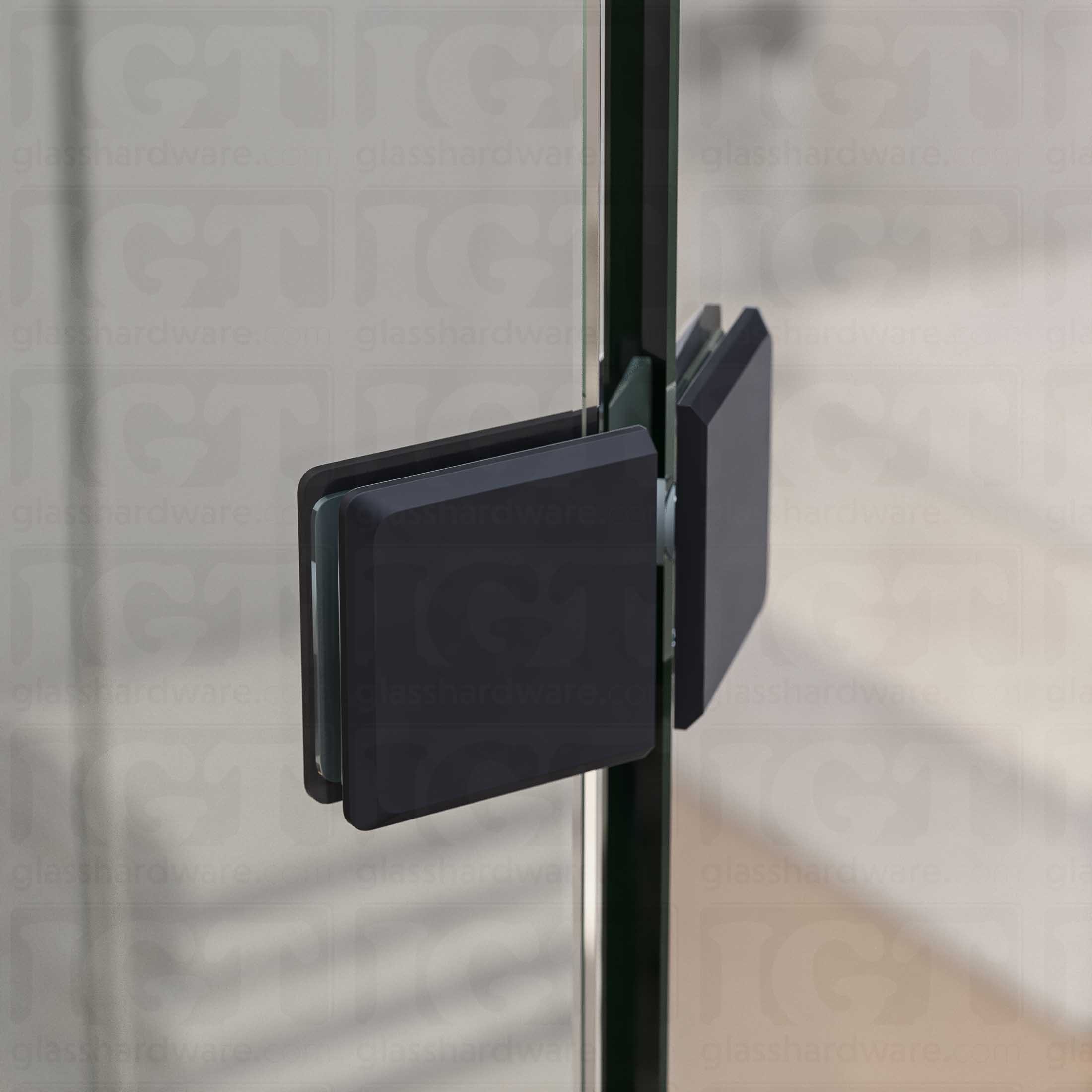 A close-up view of the Glass-to-Glass 135 Degree Bilboa Clamp, installed on a neo angle shower enclosure. The clamp's Solid Brass construction provides a secure and durable joint for the shower's angled panels. Matte Black.