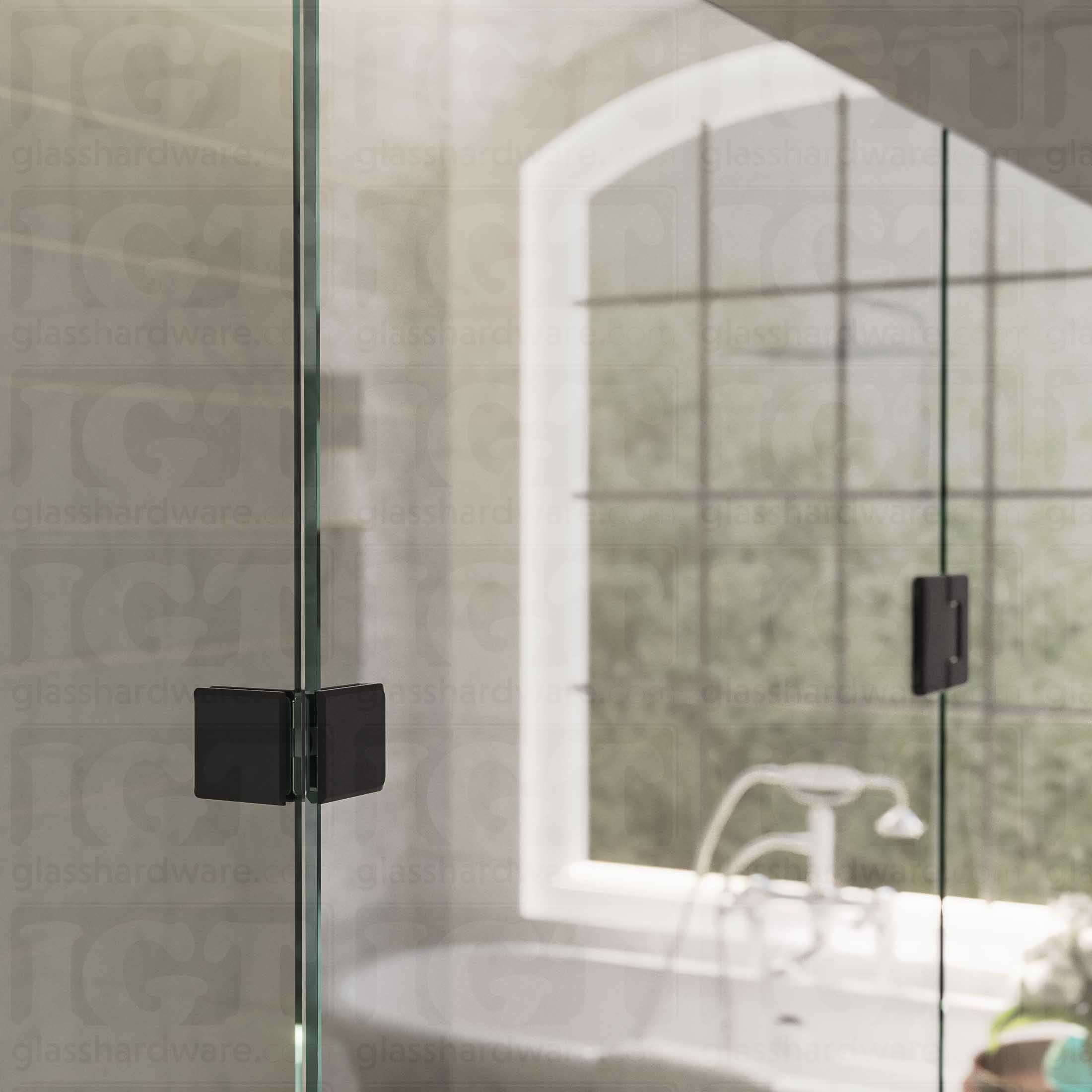 An upper view of the shower's glass panels, secured with a Glass-to-Glass 90 Degree Bilboa Clamp alongside a matching hinge. The hardware's corresponding finishes and beveled-edge design give the shower elegance and cohesiveness. Matte Black.