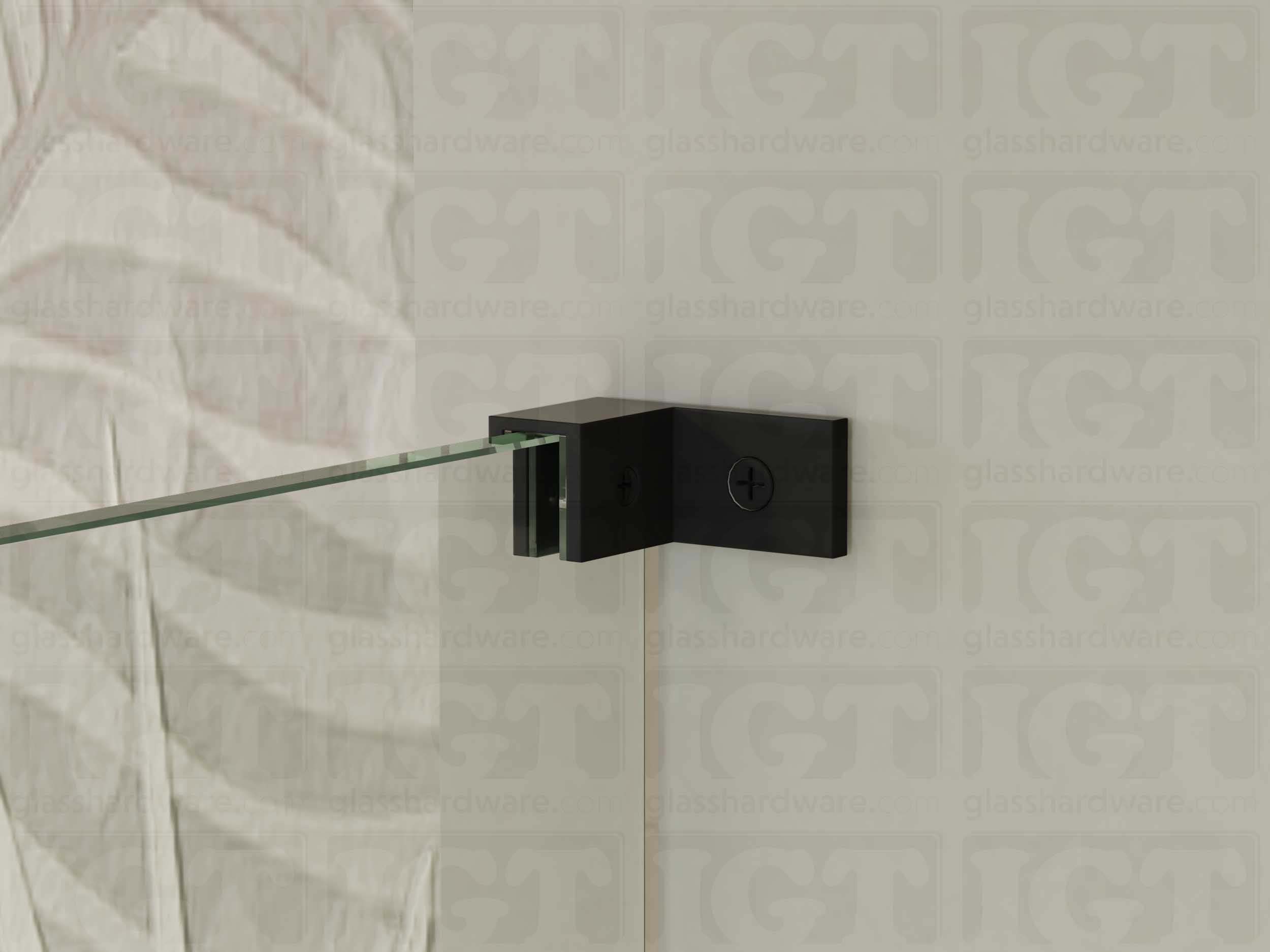 A close up of the Left Wall-to-Glass Sleeve Over Clamp installed on a frameless glass shower enclosure. The clamp is securely mounted to the shower's wall, providing additional support to the overall installation. Matte Black.