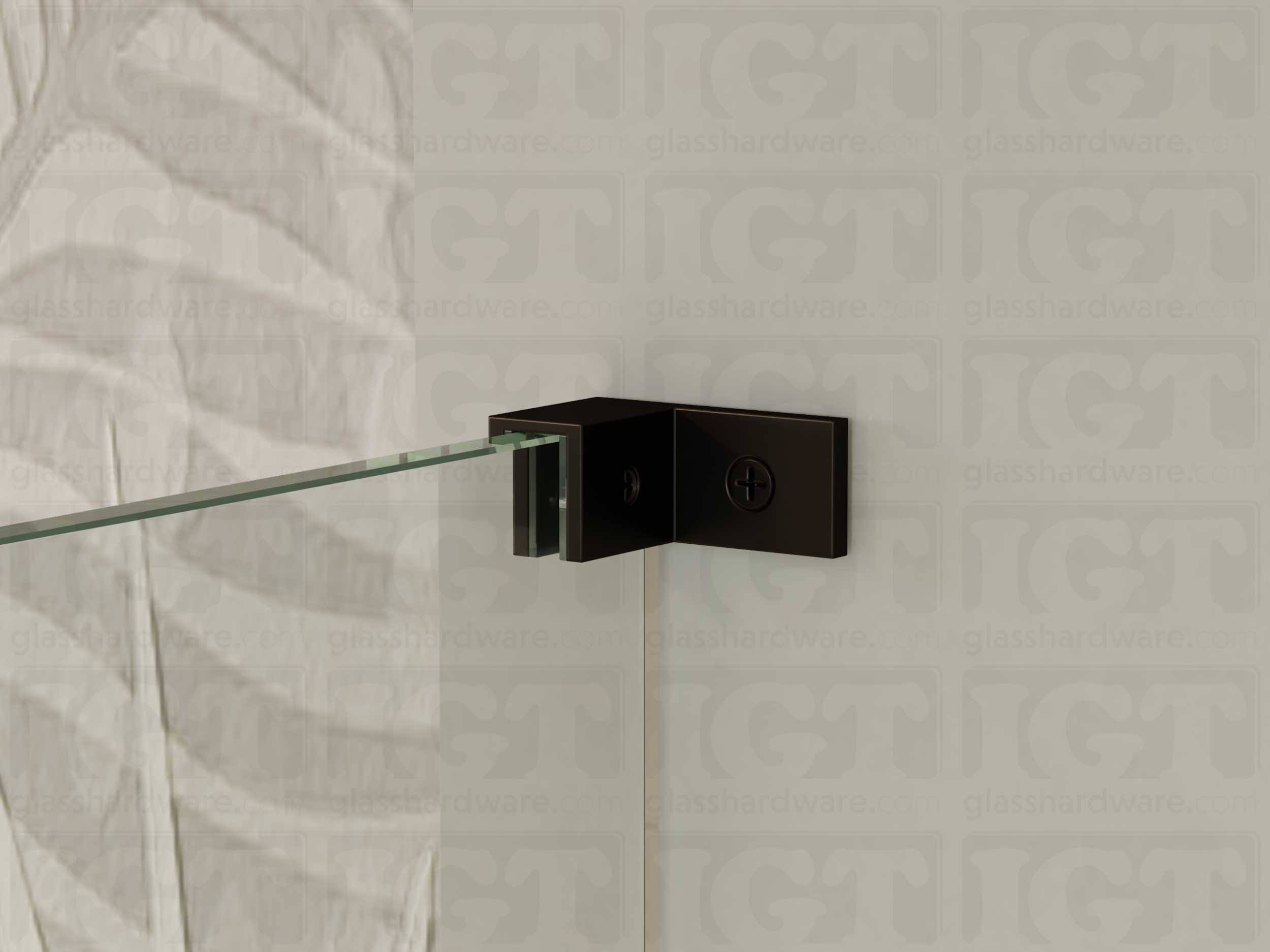 A close up of the Left Wall-to-Glass Sleeve Over Clamp installed on a frameless glass shower enclosure. The clamp is securely mounted to the shower's wall, providing additional support to the overall installation. Oil Rubbed Bronze.