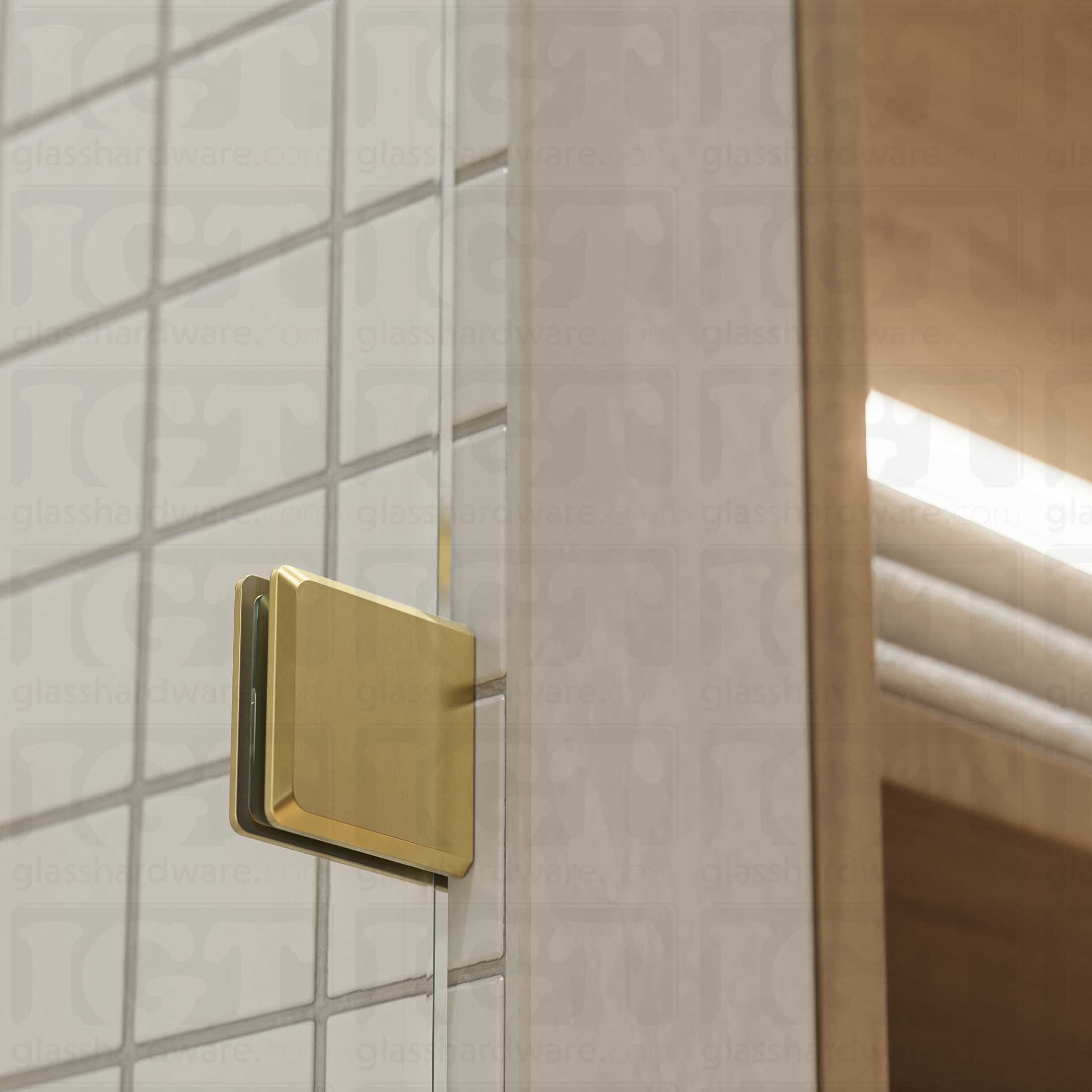 A close-up of a Wall-to-Glass Bilboa Clamp mounted to the shower's tile wall. The clamp is securely holding the shower's fixed glass panel in place. Gold Brushed.