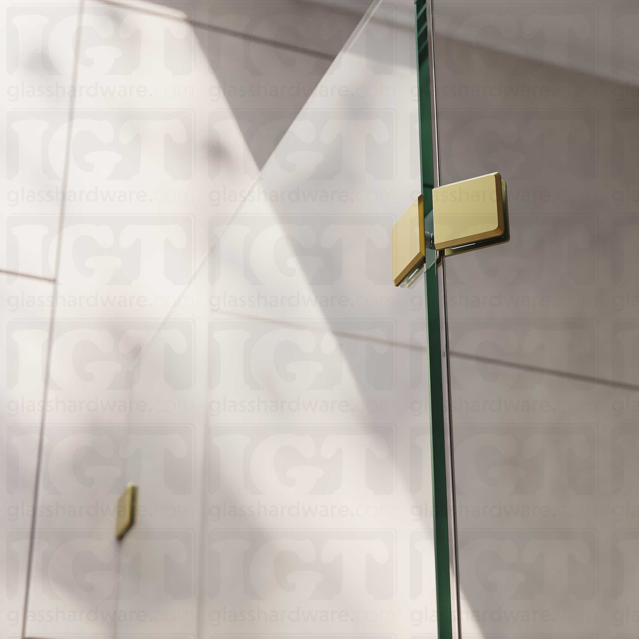 A close-up view of the Glass-to-Glass 135 Degree Bilboa Clamp, installed on a neo angle shower enclosure. Natural lighting showers in from the bathroom's window, and glistens along the clamp's sleek beveled edges. Gold Brushed.