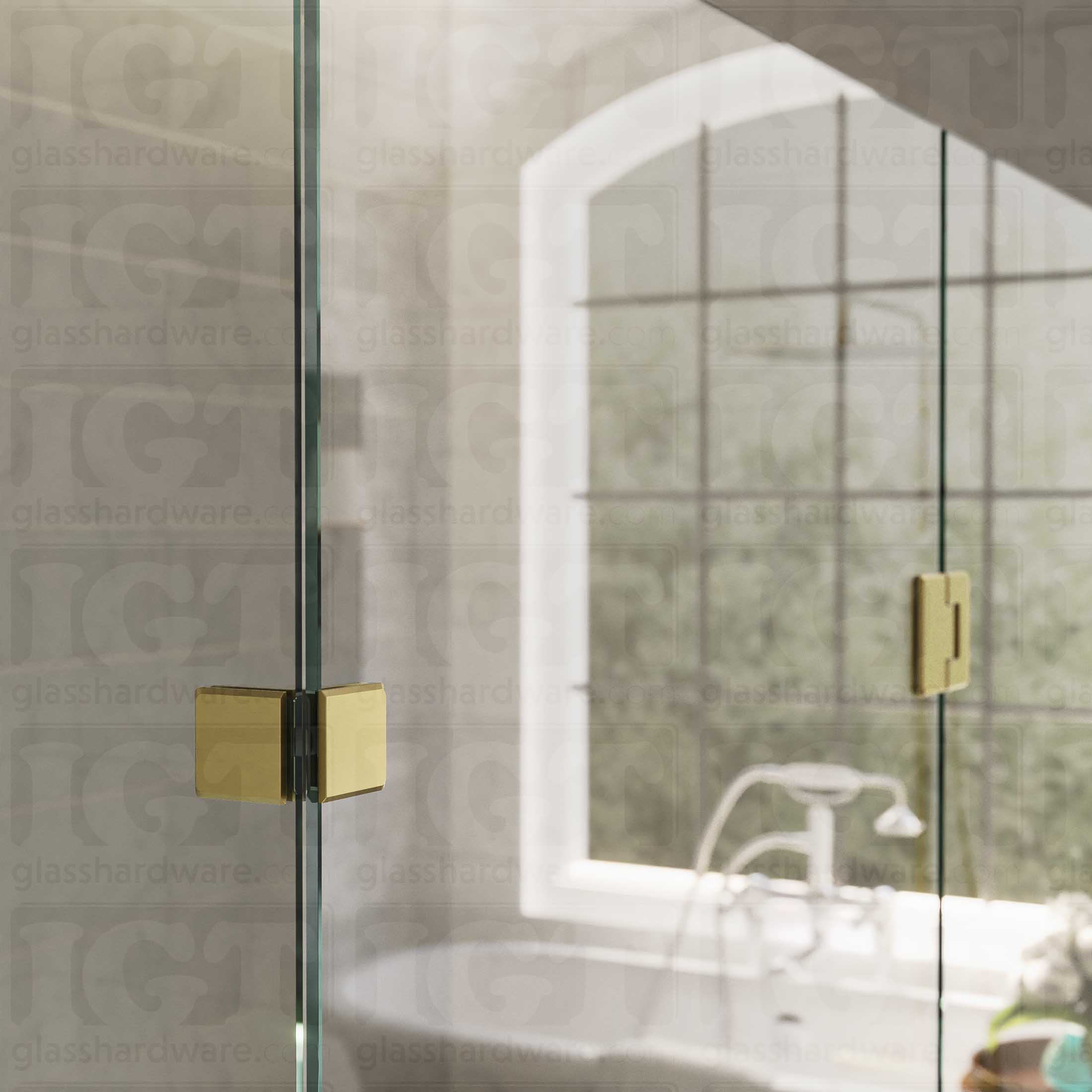 An upper view of the shower's glass panels, secured with a Glass-to-Glass 90 Degree Bilboa Clamp alongside a matching hinge. The hardware's corresponding finishes and beveled-edge design give the shower elegance and cohesiveness. Gold Brushed.