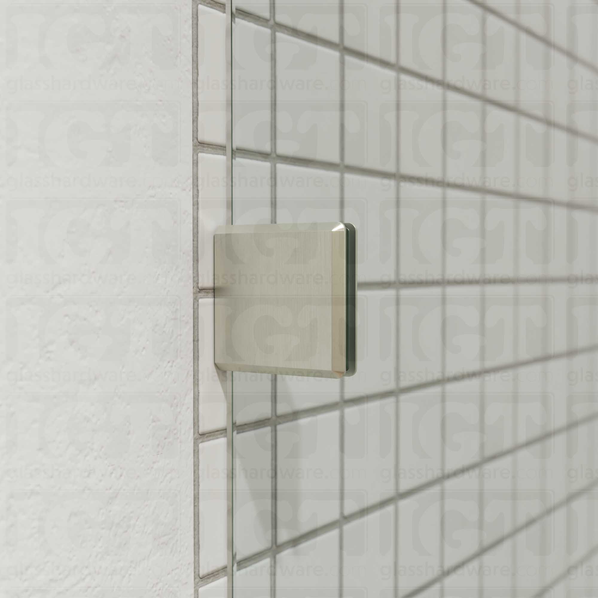 A close-up of an Oversized Wall-to-Glass Bilboa Clamp mounted to the shower's tile wall. The clamp is securely holding the shower's fixed glass panel in place. Brushed Nickel.