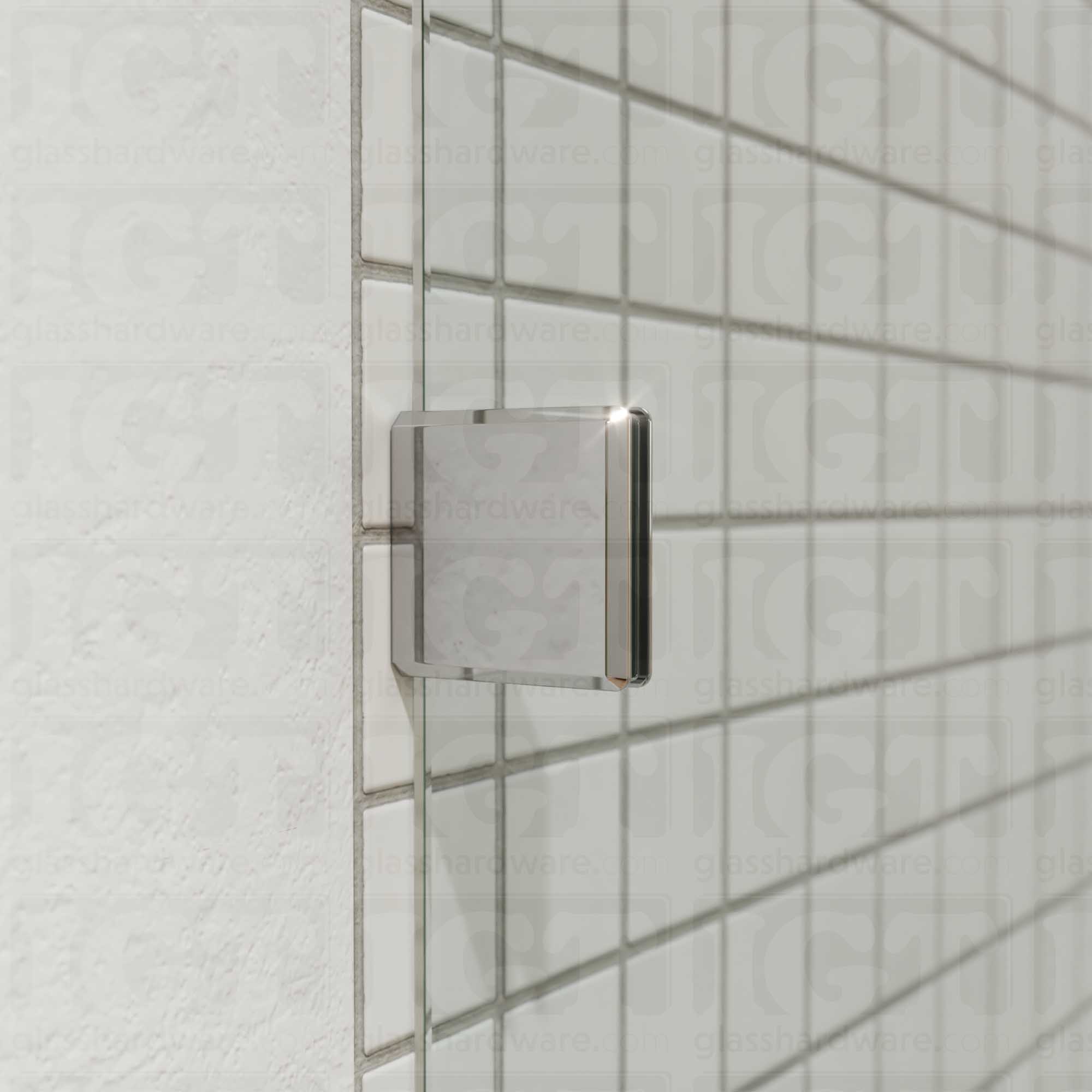 A close-up of an Oversized Wall-to-Glass Bilboa Clamp mounted to the shower's tile wall. The clamp is securely holding the shower's fixed glass panel in place. Chrome Polished.