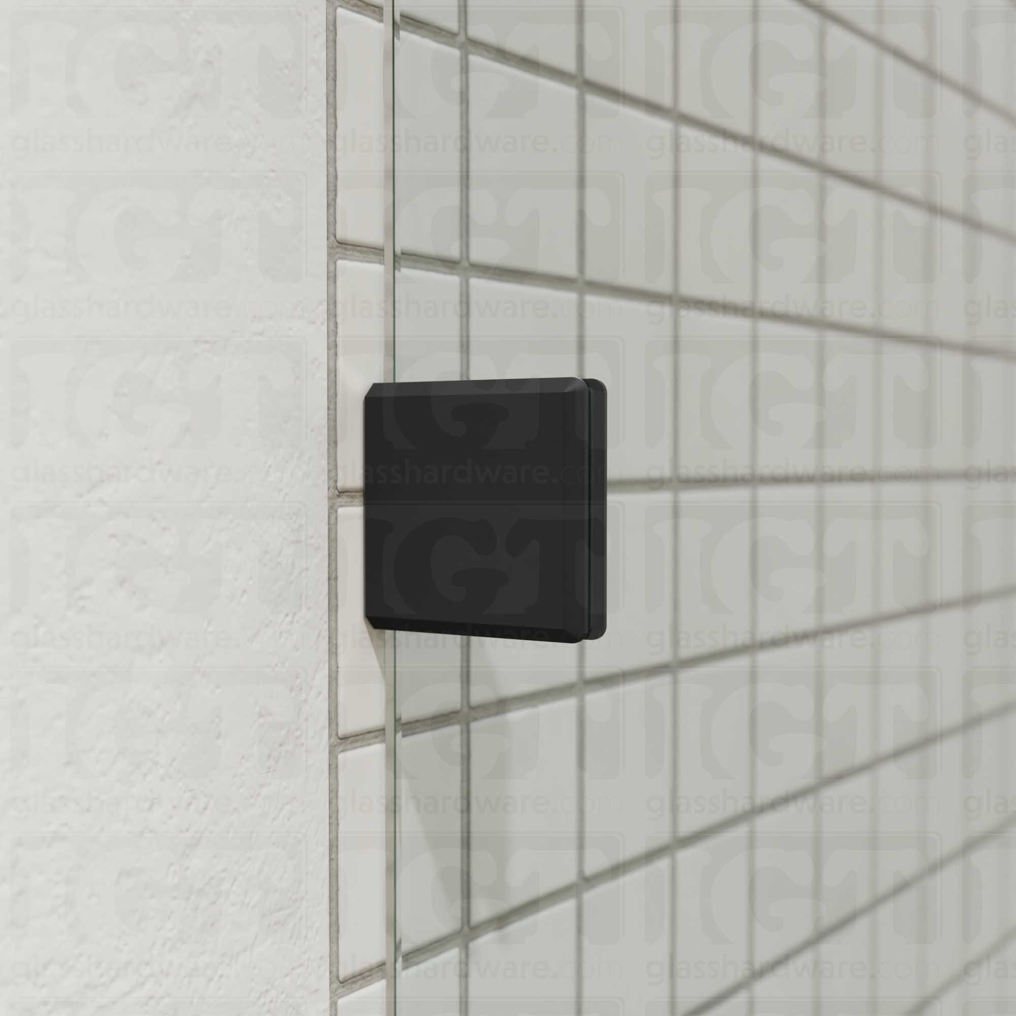 A close-up of an Oversized Wall-to-Glass Bilboa Clamp mounted to the shower's tile wall. The clamp is securely holding the shower's fixed glass panel in place. Matte Black.