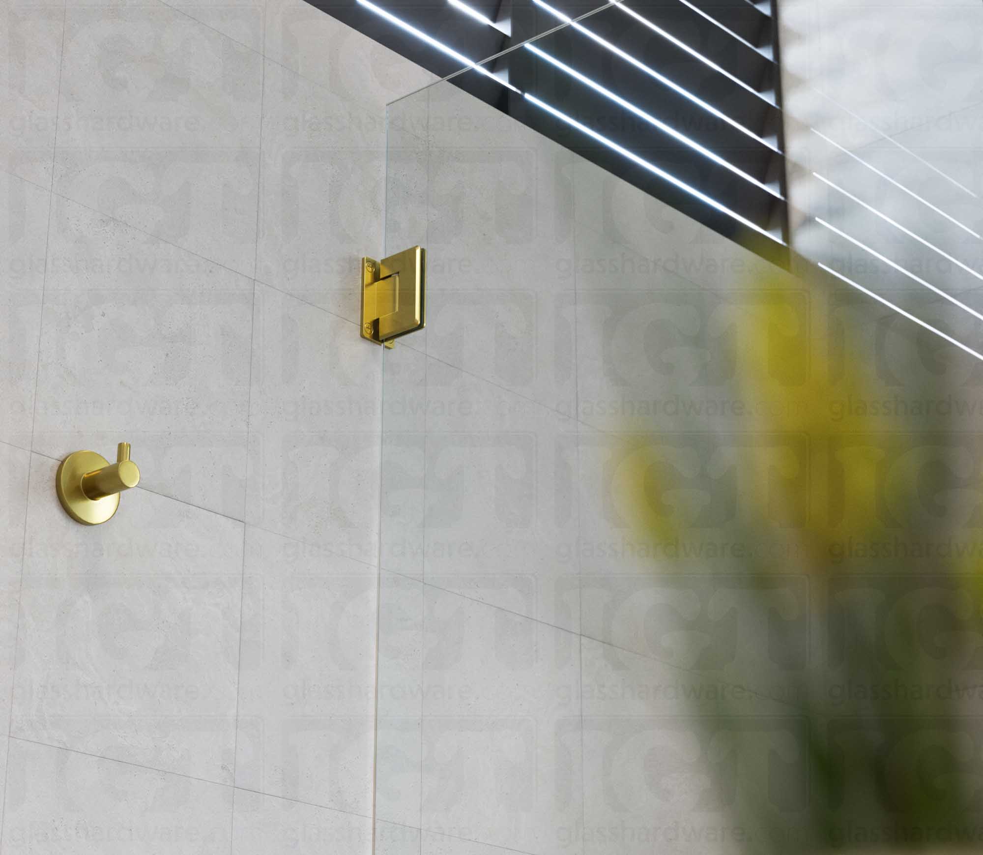 A close-up view from below of the Wall-to-Glass Full Back Bilboa Hinge used in a modern shower door installation. Gold Brushed.