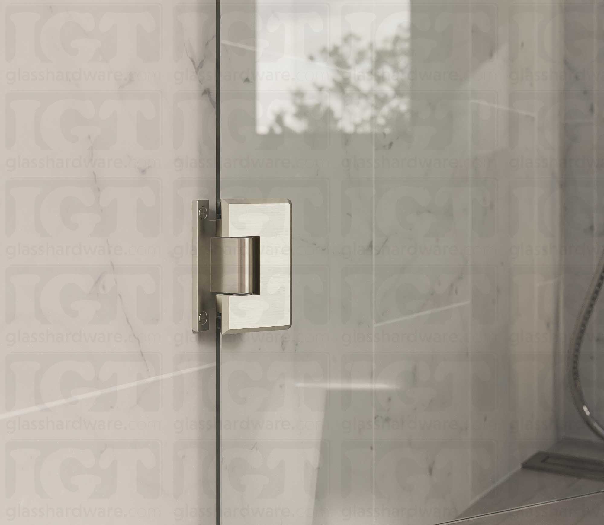 A close up view of the Heavy Duty Wall-to-Glass “H” Back Bilboa Hinge installed on a frameless glass shower door. The bathroom's natural lighting reflects along the hinge's sleek beveled edges, adding dimension to the overall design. Brushed Nickel.