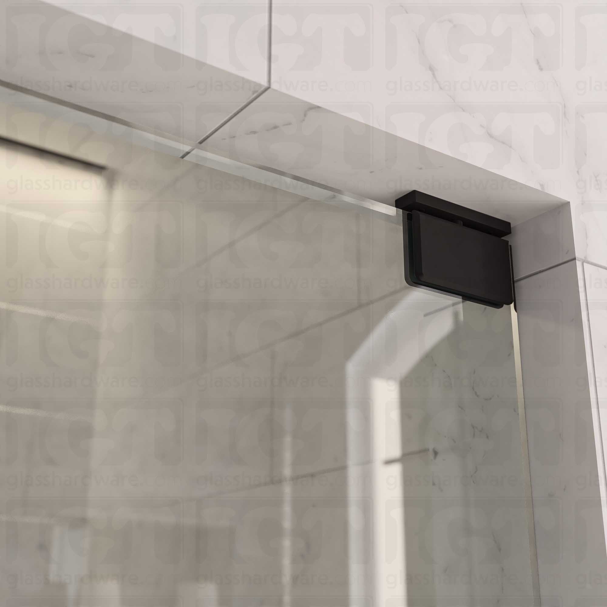 Close-up of the Top and Bottom Bilboa Pivot Hinge mounted at the top of the glass shower door, securing it to the tiled wall. The hinge has soft rounded corners and beveled edges, making it blend into the elegant bathroom setting. Matte Black.